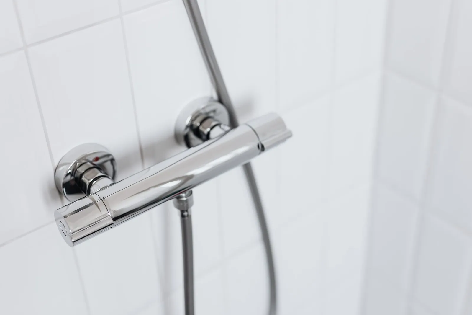 Chrome thermostatic shower mixer on a white tiled wall