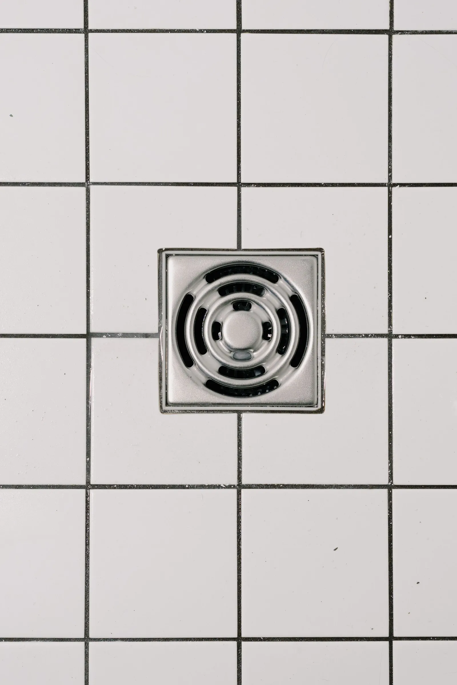 Stainless steel shower drain set in white floor tiles