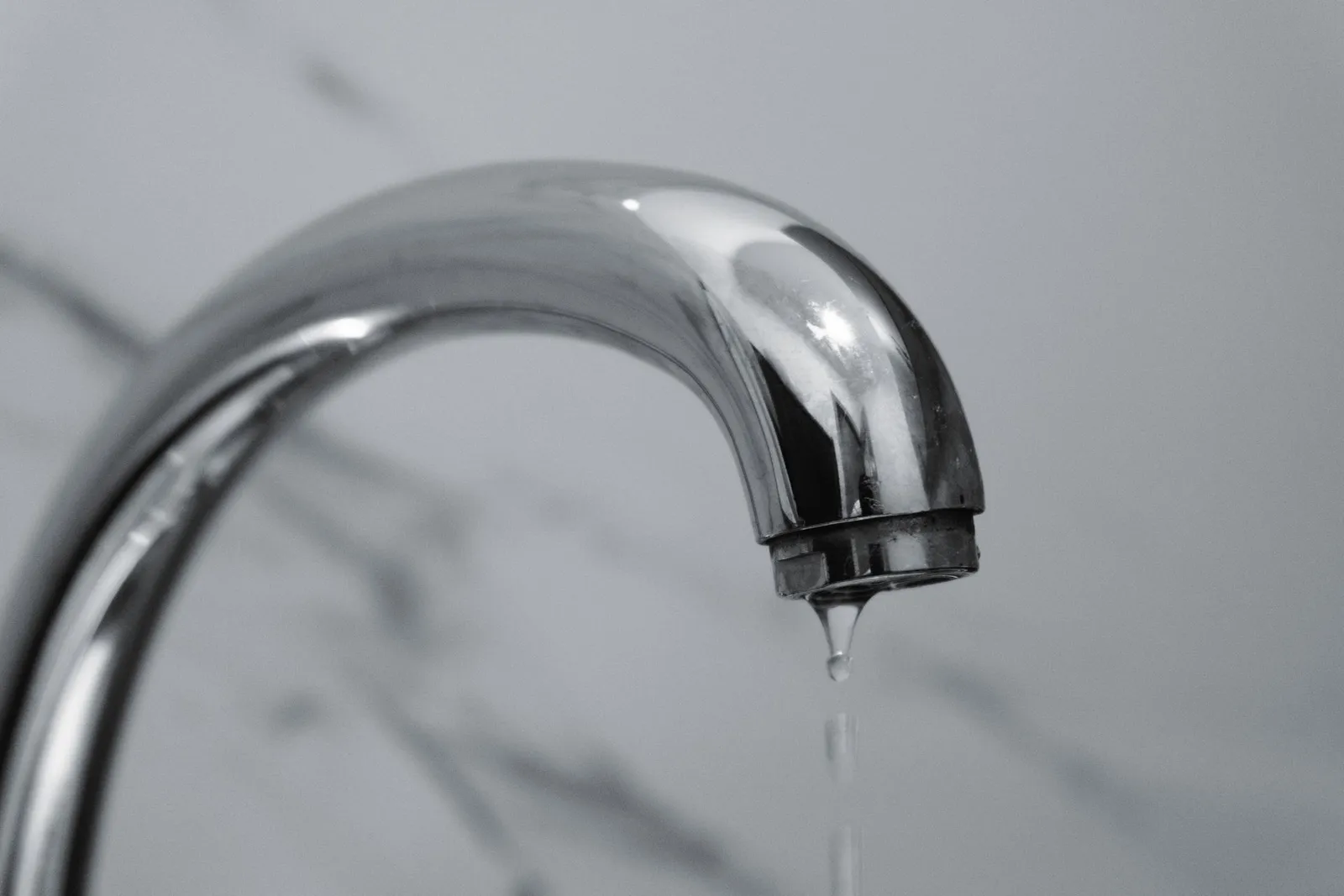 Chrome tap dripping water against grey marble